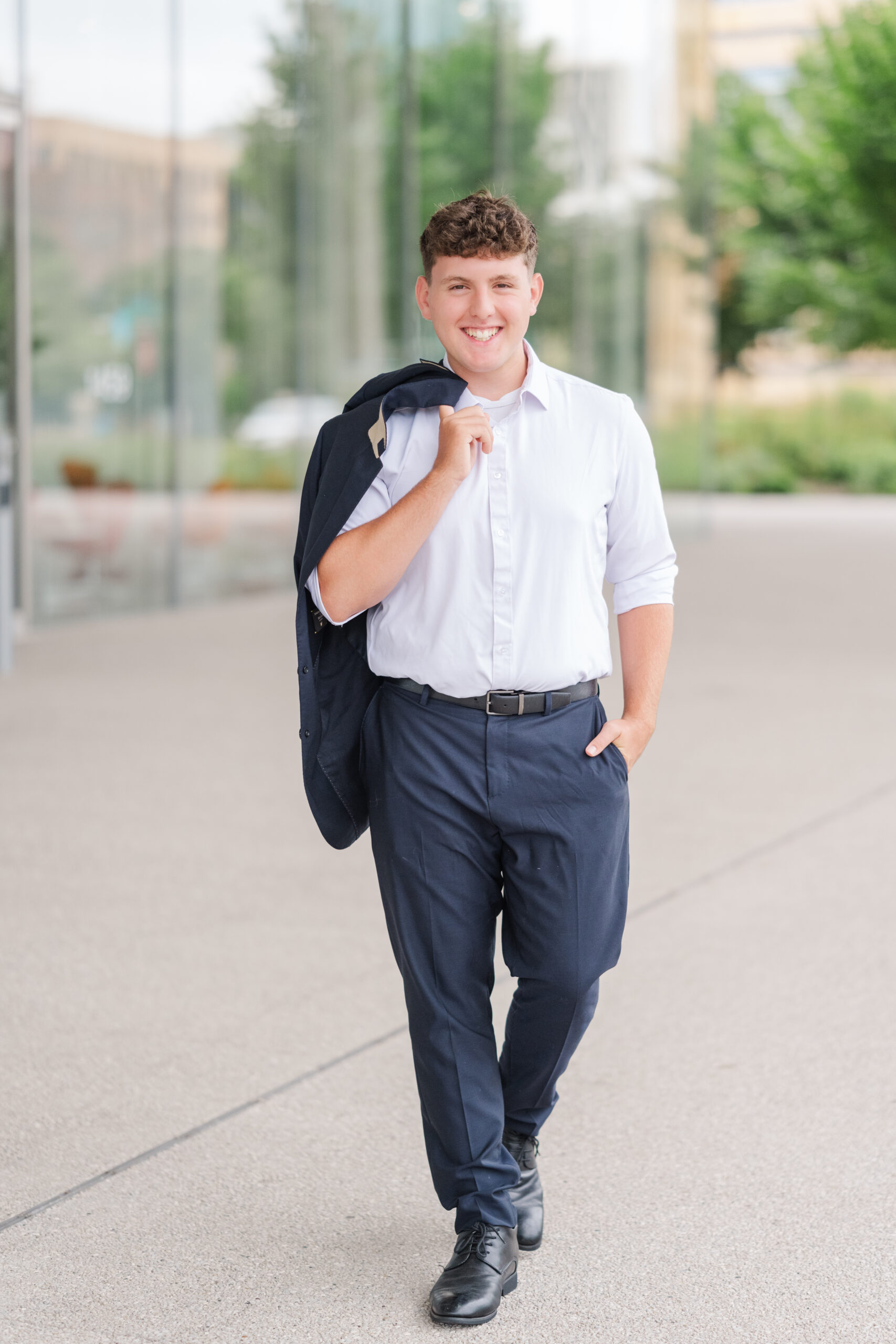 a high school senior male walks towards the camera with suit coat draped over shoulder