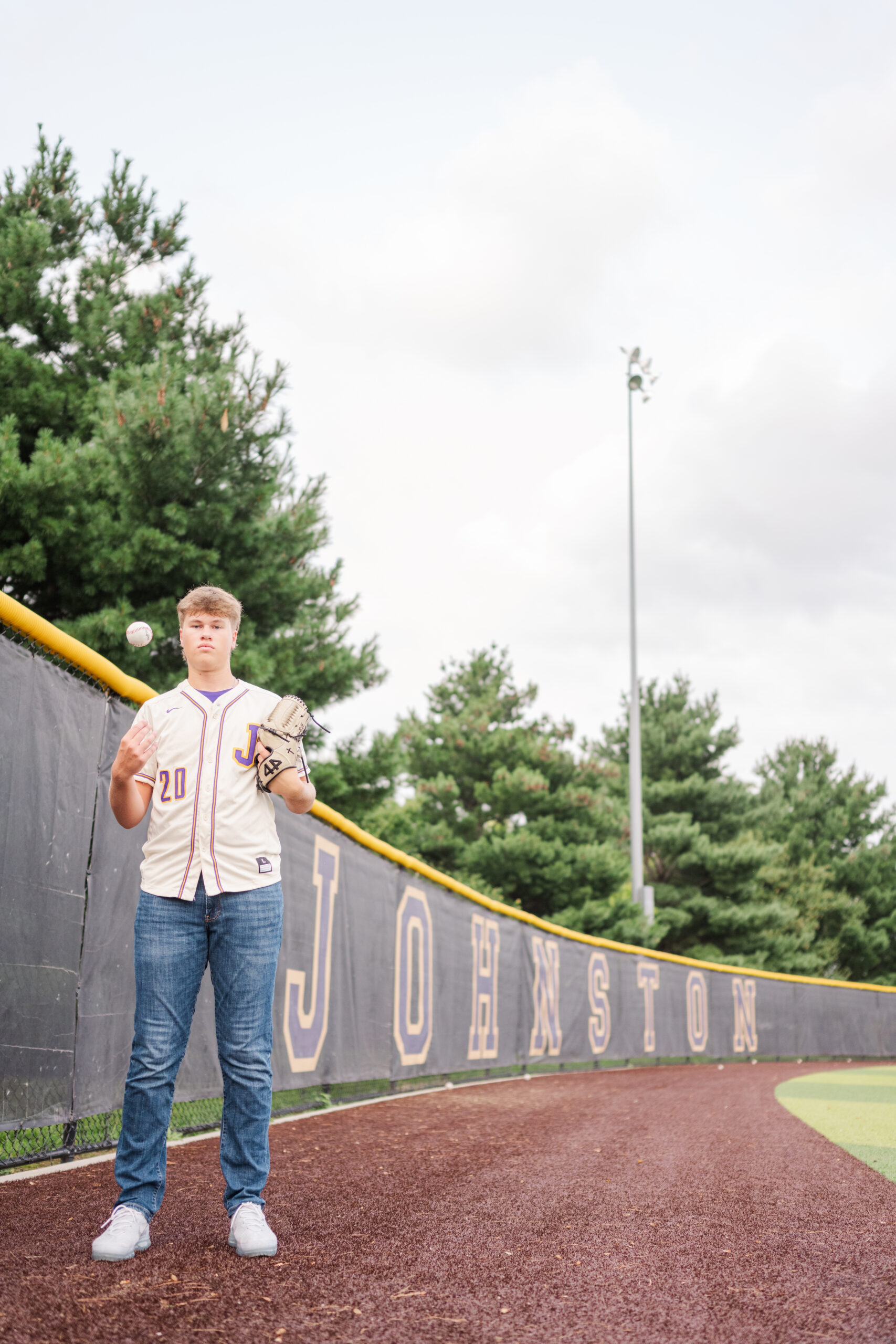 a high school pitcher stands in the outfield next to the Johnston banner